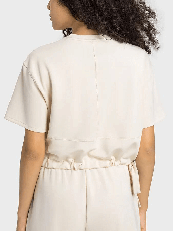 Woman wearing a cream sports short sleeves crop T-shirt with adjustable hem from back view, showcasing breathable, quick-dry fabric.